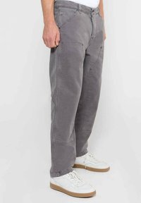 Grijze katoenen broek met een relaxed fit, voorzien van een platte voorkant, zijzakken en een licht taps toelopend ontwerp. G gedragen met witte sneakers.