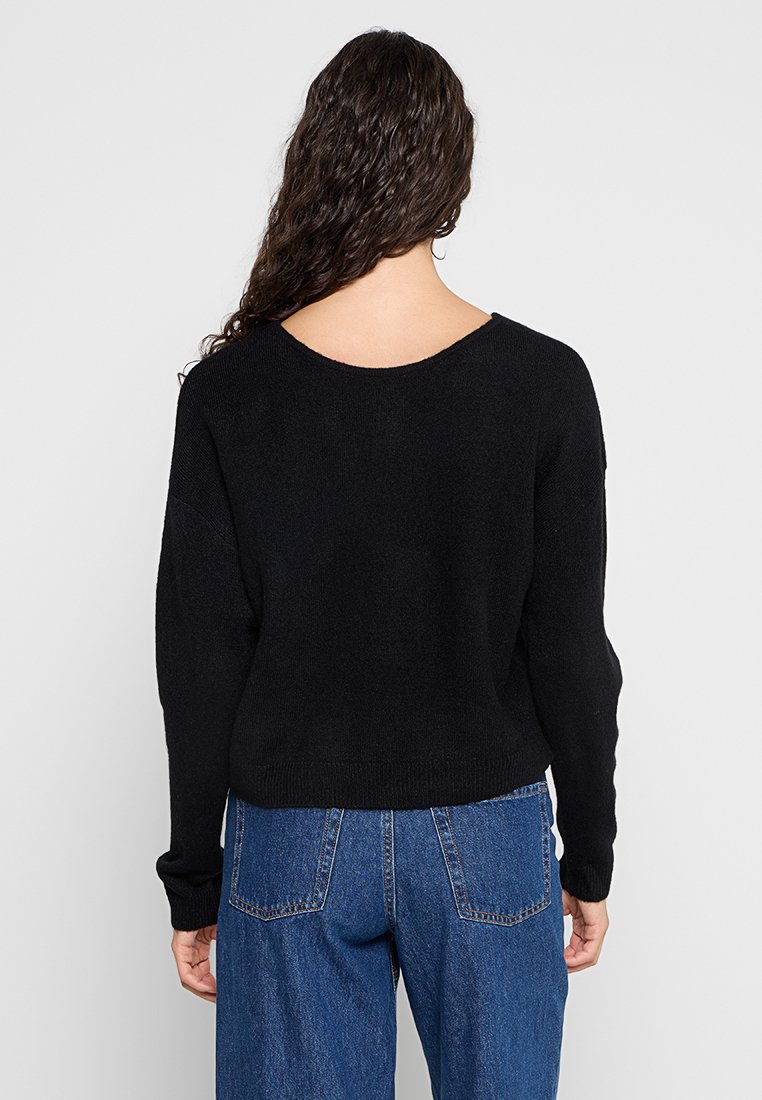 Sweater nero lavorato a maglia con scollo ampio, spalle scese e orlo a coste. Abbinato a jeans blu a vita alta, con un fit rilassato.