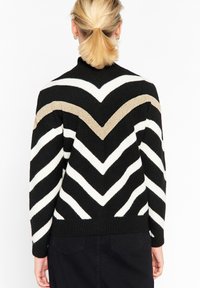 Suéter de patrón de chevron en blanco y negro con acentos en dorado, que cuenta con un cuello alto y un tejido texturizado. Corte ajustado con puños y dobladillo acanalados.