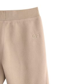 I pantaloni jogger in pile beige presentano una vita a coste e un logo discreto con due facce sorridenti. Il tessuto sembra morbido e accogliente.