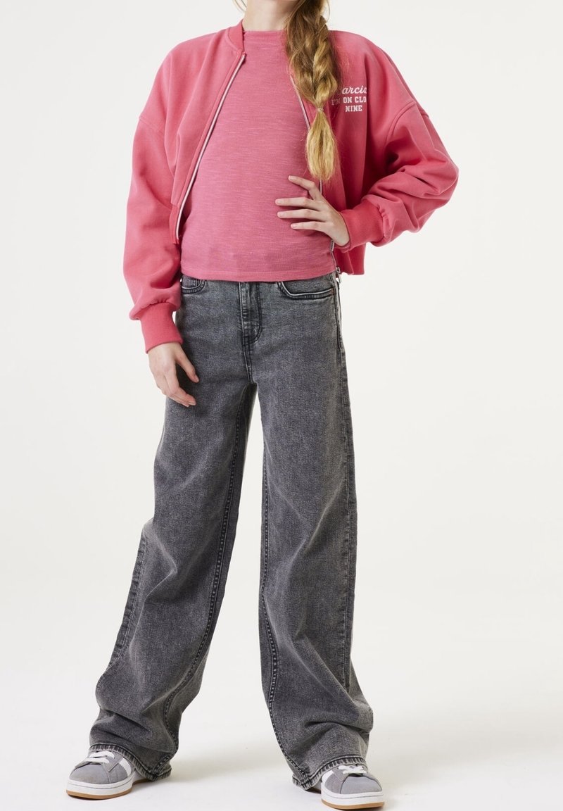 Felpa corta rosa con texture a coste, abbinata a jeans grigi sbiaditi a gamba larga. Le scarpe sono grigie con accenti e lacci bianchi.