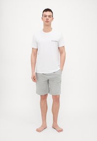 Weißes T-Shirt mit kurzen Ärmeln und Logo auf der Brust, kombiniert mit grauen Baumwollshorts. Lässige Passform, keine Muster, schlichte Texturen und weicher Stoff.