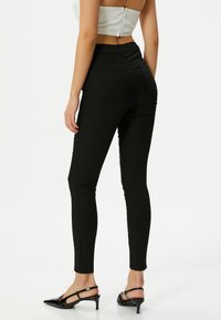 Jeans skinny negros con un diseño ajustado, textura suave, cintura de altura media y bolsillos traseros. Combinados con unos tacones tipo slingback negros.