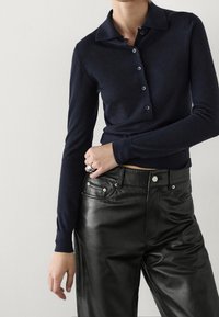 Tummansininen pitkähihaisella kauluspaita, jossa on kaulus ja viisi nappia, yhdistetty mustiin nahkahousuihin. Kangas näyttää pehmeältä ja hieman teksturoidulta.