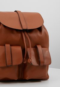 Brauner Leder-Rucksack mit einer strukturierten Oberfläche, einer Klappenverschluss und zwei Fronttaschen. Verfügt über eine Kordelzug und kontrastierende Nähte.