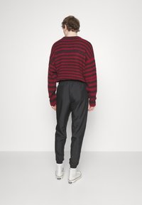 Red and black striped knit sweater paired with black elastic-waist joggers and white high-top sneakers, viewed from the back.