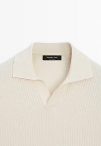 Polo en maille côtelée couleur crème avec col ouvert, avec une étiquette Massimo Dutti à l’intérieur de l’encolure.