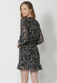 Rochie neagră cu flori, cu mâneci lungi din material transparent, talie elastică și tiv volanat. Prezintă un model cu flori albastre, portocalii și crem.