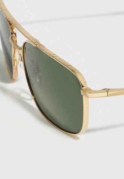 Κοντινό πλάνο γυαλιών ηλίου με χρυσό μεταλλικό πλαίσιο, πράσινους φακούς και διακριτικά χαραγμένα σχέδια στις άκρες του πλαισίου και στα μπράτσα.