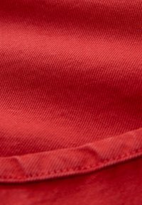 Primo piano di un tessuto rosso con una trama liscia e opaca e un bordo piegato con dettaglio di cuciture a contrasto.