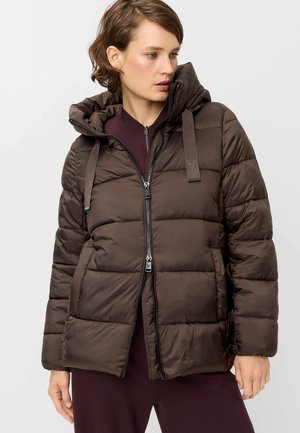 Woman wearing a dark brown quilted puffer jacket with hood and zipper, looking to the side, against a plain light background.
