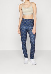 Blå mönstrade sweatpants med palmblad design, elastisk midja, sidofickor, tillsammans med en beige sport-bh och vita sneakers.