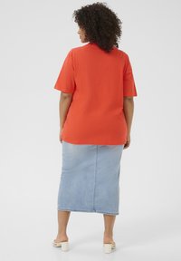 T-shirt orange à manches courtes associé à une jupe en denim léger. Le t-shirt a une coupe décontractée, tandis que la jupe présente une coupe droite classique.