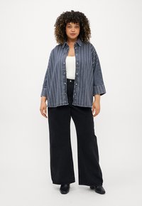Denim oversize krekls ar zilām vertikālām svītrām, ar pogām priekšpusē un manšetes piedurknēm, kombinēts ar augsto jostu melnām platām biksēm.