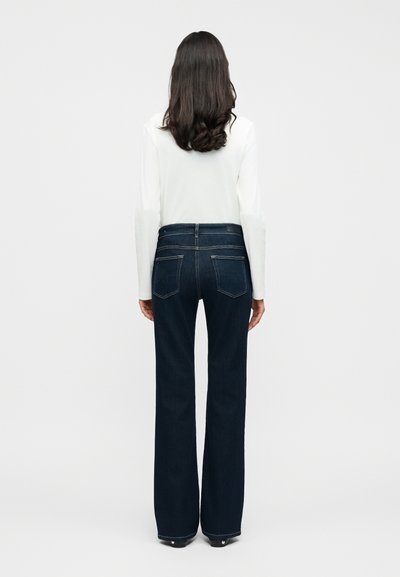 Σκούρα μπλε τζιν με καμπάνες και ψηλή μέση, με ορατή ραφή, δύο πίσω τσέπες και λείο υλικό από denim. Άσπρο τοπ ορατό στη μέση.