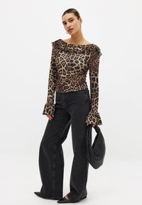 Long-sleeve, leopard print blouse with ruffled neckline, paired with high-waisted black jeans and pointed-toe black shoes. Textured woven bag.