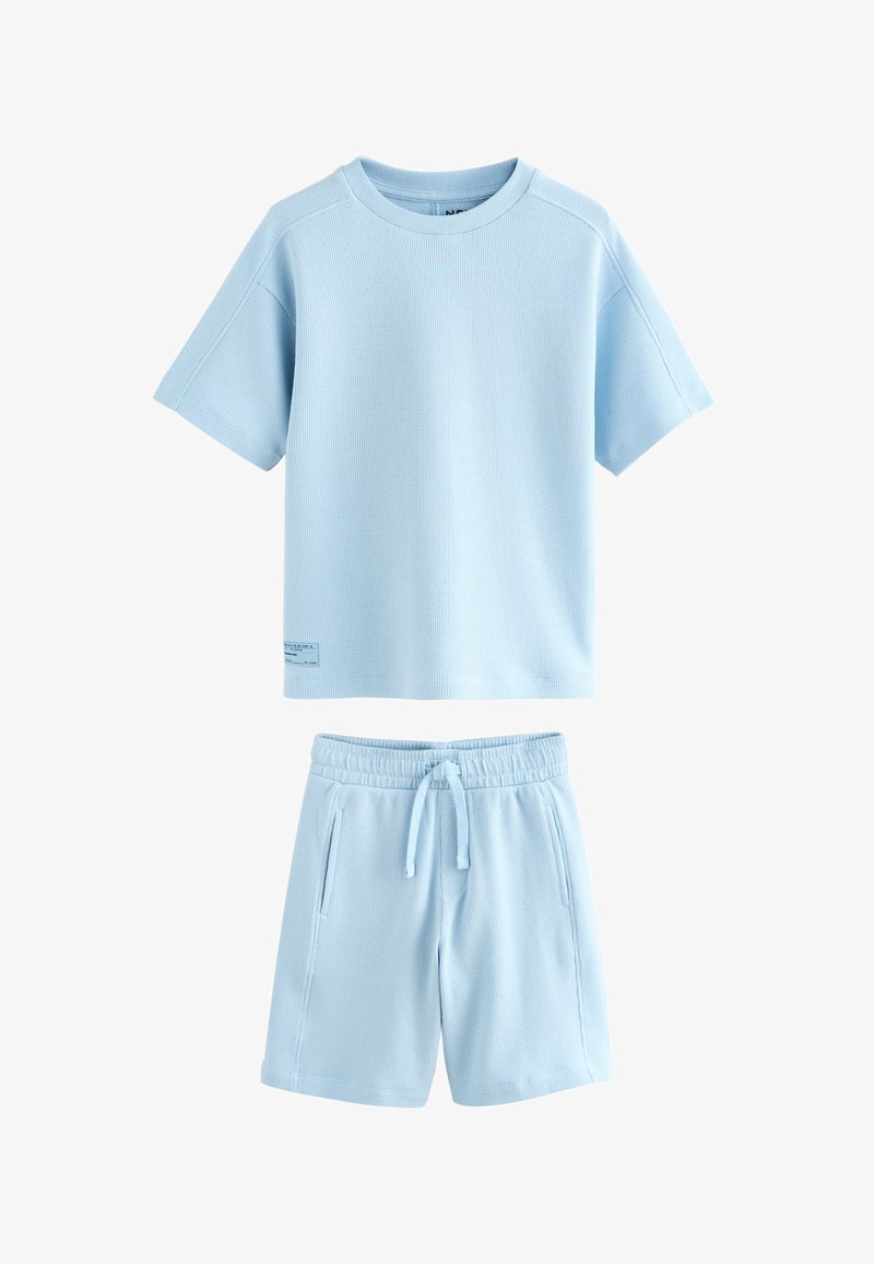 Completo composto da maglietta a maniche corte a coste waffle color azzurro chiaro e pantaloncini coordinati con coulisse e tasche laterali.