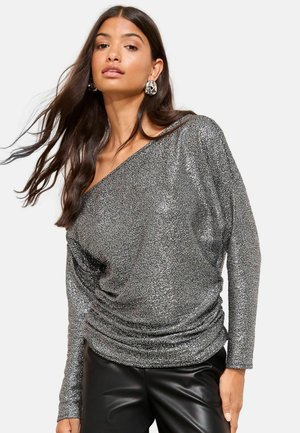 Metallisk silverfärgad off-shoulder topp med draperad tyg, långa ärmar och en mjuk textur. Bärs med åtsittande svarta läderbyxor.