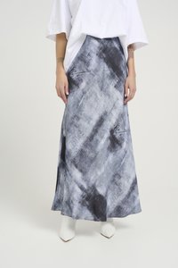 Saia longa e fluída em padrão abstrato cinza e preto, feita de tecido leve. Apresenta uma fenda lateral e combina com botas brancas de bico fino.