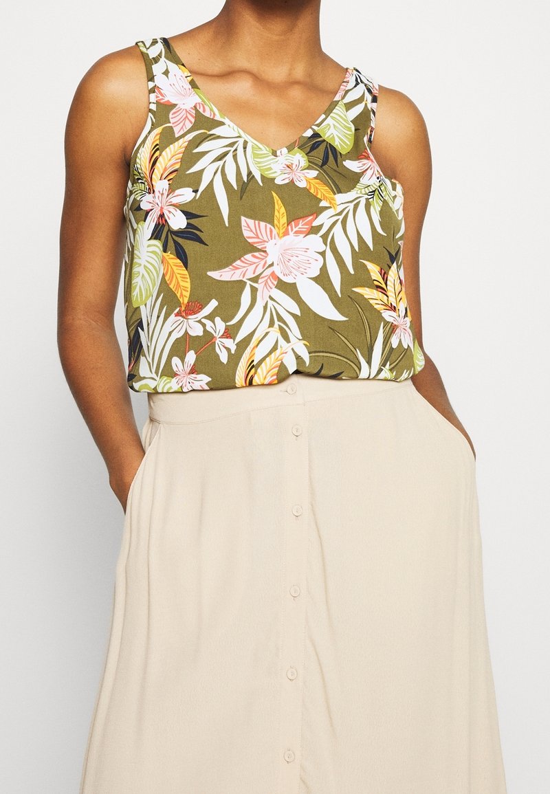 Débardeur vert à motifs floraux avec un col en V, présentant des fleurs roses, blanches et jaunes. Associé à une jupe crème à boutons sur le devant.