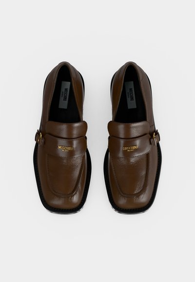 Paire de mocassins en cuir marron Moschino Milano avec logo doré à l'avant et semelles noires, vus de dessus sur fond blanc.