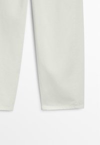 Unterer Bereich von hellbeigen, gerade geschnittenen Hosen mit sichtbaren Nähten und sauberen Säumen vor weißem Hintergrund.