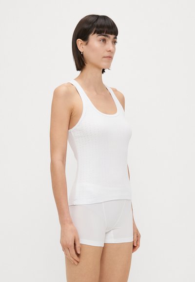 Balts ribots tvertnes topiņš ar apaļu kakla izgriezumu, šaurām siksnām un teksturētu rakstu. Valkāts kopā ar baltām pieguļošām šortiem. Gluda, viegla auduma.