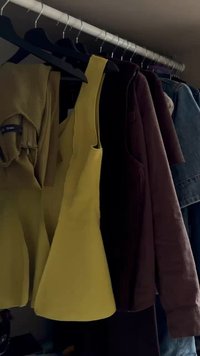 Three tops hanging on hangers: a yellow sleeveless top, a brown long-sleeve shirt, and a denim jacket. Diverse textures and colors visible.