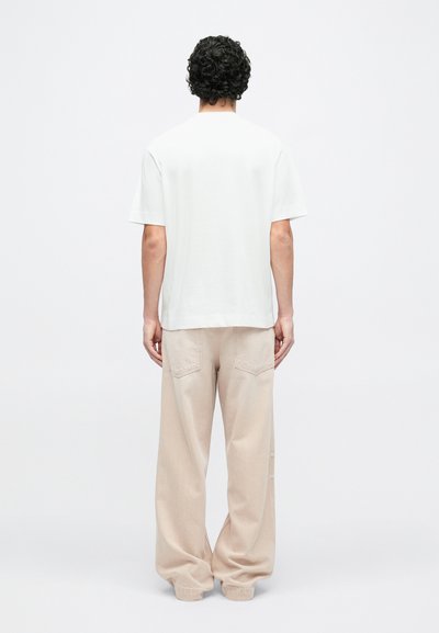 Biele tričko s uvoľneným strihom, krátkymi rukávmi a rovnou lemom, skombinované s béžovými širokými nohavicami s zadnými vreckami a manžetami na nohaviciach.