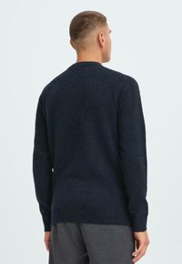 Dunkelblauer Herrenpullover mit langen Ärmeln, Rundhalsausschnitt, strukturiertem Strick und geripptem Saum, von hinten gegen einen hellen Hintergrund gezeigt.