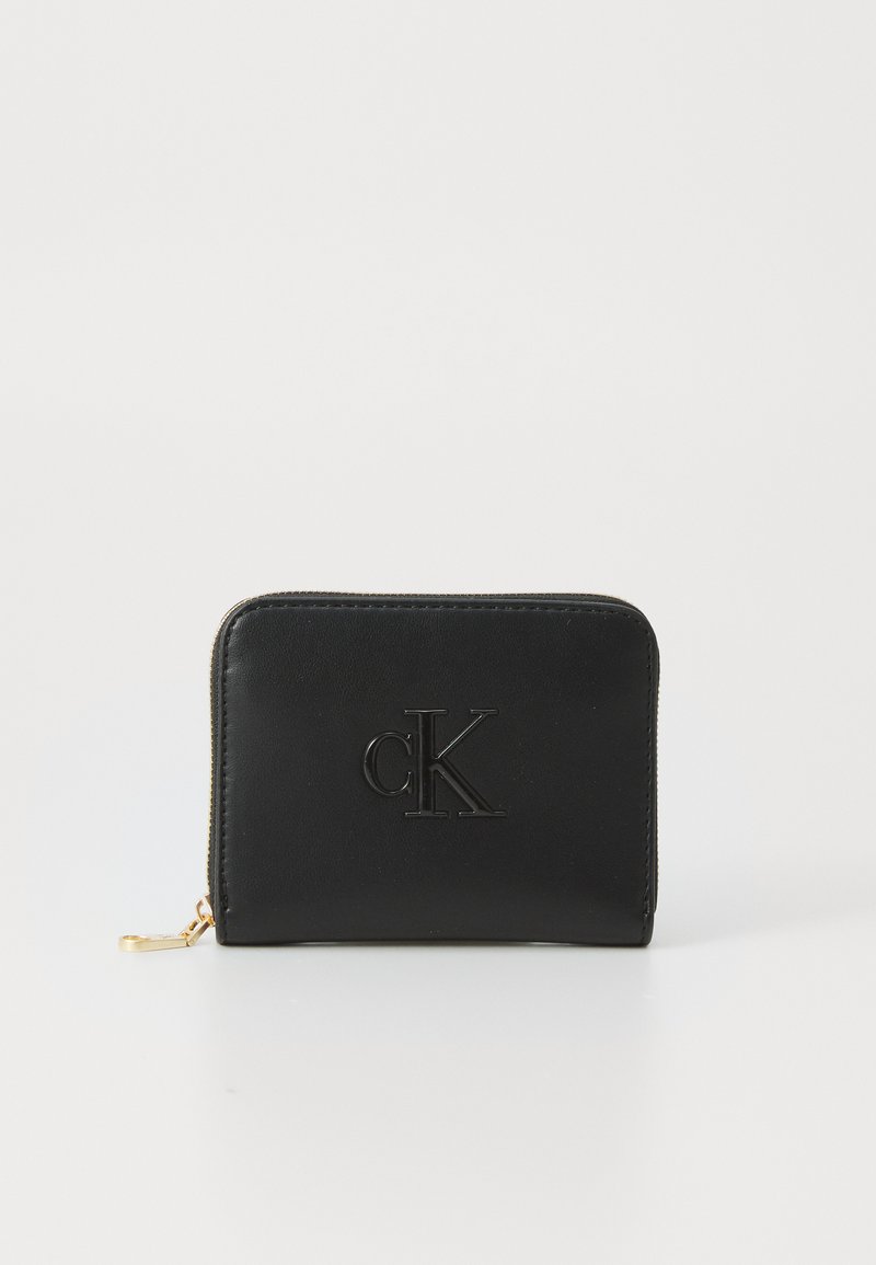 Portofel din piele neagră cu logo-ul „cK” embosat, închidere cu fermoar și accente de hard disk aurii. Textură netedă, cu o formă rectangulară.