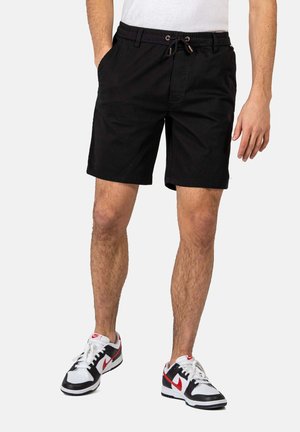 Black shorts made of cotton with an elastic waistband and drawstring. Features two side pockets and a straight hem. Paired with black and white sneakers.