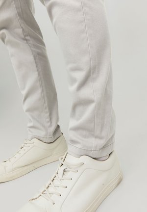 Pantalon gris clair en mélange de coton, présentant une silhouette ajustée et des coutures minimales, associé à des baskets blanches.