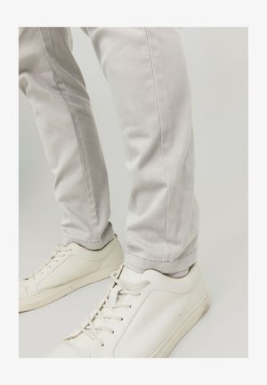 Pantalones gris claro de mezcla de algodón, con un corte ajustado y costuras mínimas, combinados con zapatillas blancas.