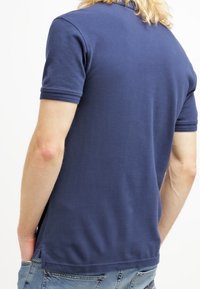 Granatowa koszulka polo wykonana z bawełny, z krótkimi rękawami, płaskim kołnierzykiem i bocznymi rozcięciami na dole, które ułatwiają ruch.