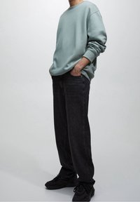 Sudadera verde claro de manga larga, con un ajuste holgado; combinada con jeans oscuros de color gris. Zapatillas negras completan el atuendo casual.