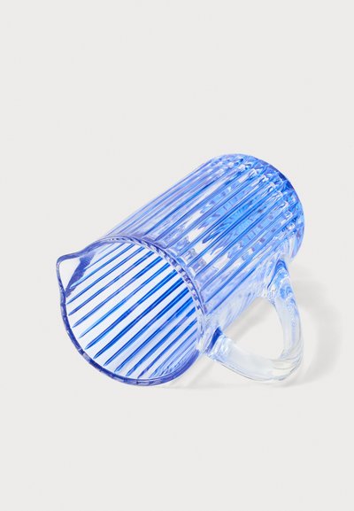 Pichet doseur en plastique bleu transparent avec des rainures verticales et une poignée, présenté couché sur le côté sur une surface blanche.