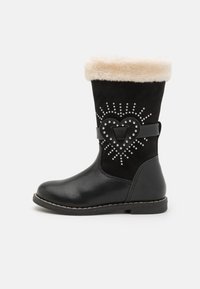 Bottine noire avec poignet en fausse fourrure, embellie de clous en forme de cœur et d'une sangle décorative. Matériaux en cuir lisse et en daim texturé.
