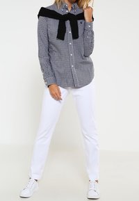 Black and white checkered button-up shirt, with a black sweater tied around the shoulders, paired with white pants and white sneakers.