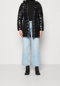 Sort puffermantel med hætte, der har en blank finish og lodret quiltet design, kombineret med lyseblå viddebukser og sorte ankelstøvler.