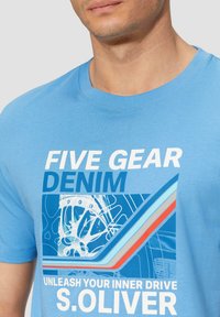 Lichtblauw T-shirt van katoen, met een grafische print met tekst en geometrische vormen in een donkerder blauw, rode en witte accenten.