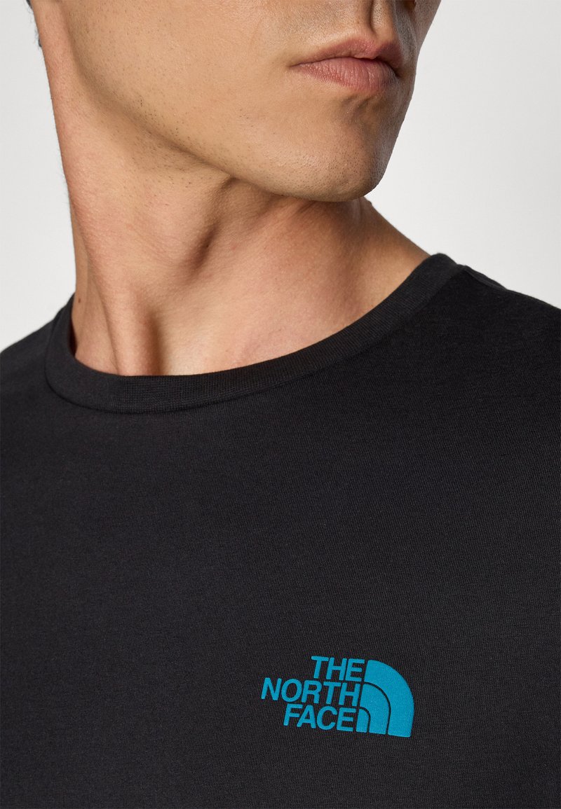 T-shirt noir avec un col rond, arborant un logo brodé bleu sur le côté gauche de la poitrine, fabriqué en coton lisse.