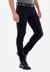 Zwarte denim jeans hebben een slim fit, vijf zakken met ton-sur-ton stitching, en worden gecombineerd met een zwart studded riem en zwarte veterschoenen.