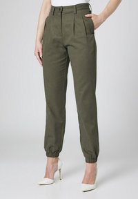 Oliwkowe, plisowane spodnie z wysokim stanem i elastycznymi mankietami, połączone z białymi szpilkami. Gładki materiał, minimalistyczny design.