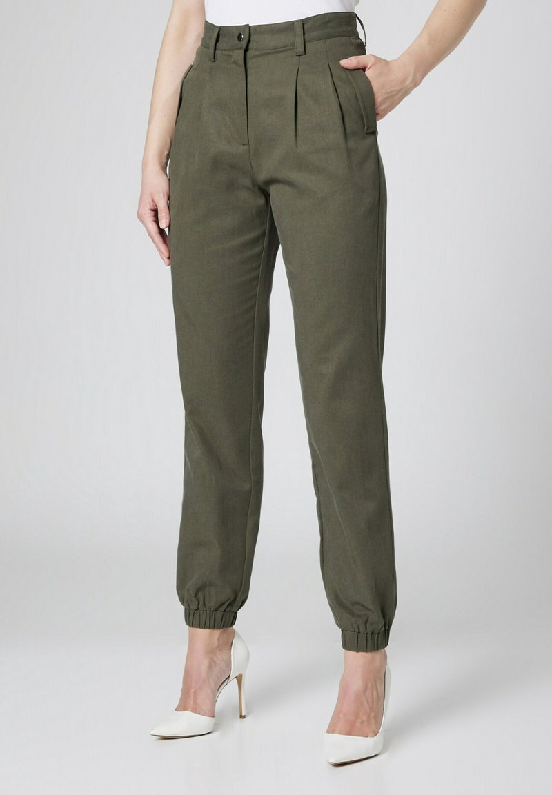 Oliwkowe, plisowane spodnie z wysokim stanem i elastycznymi mankietami, połączone z białymi szpilkami. Gładki materiał, minimalistyczny design.