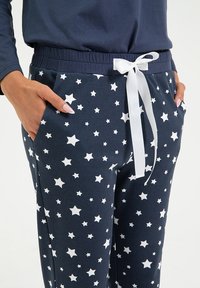 Granatowe spodnie piżamowe w białe gwiazdy, z elastycznym pasem i białą wstążką. Posiada boczne kieszenie i gładką bawełnianą tkaninę.
