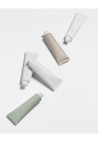 Viisi kosmetiikkaputkea eri kokoisina ja väreissä: valkoinen, beige ja vihreä; minimalistisella muotoilulla ja korkillisilla aukkoilla.