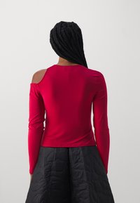 Red long-sleeve top with off-the-shoulder design. Smooth, stretchy fabric. Back view, paired with a quilted black skirt.