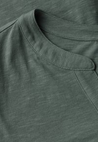 T-shirt in cotone verde con scollatura rotonda, caratterizzato da un delicato motivo a texture e una finitura liscia. Cuciture a contrasto sui bordi.
