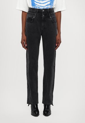 Schwarze Jeans mit hoher Taille und doppeltem Knopfverschluss, kombiniert mit einem weißen und blauen Cropped-T-Shirt und schwarzen spitzen Stiefeln.